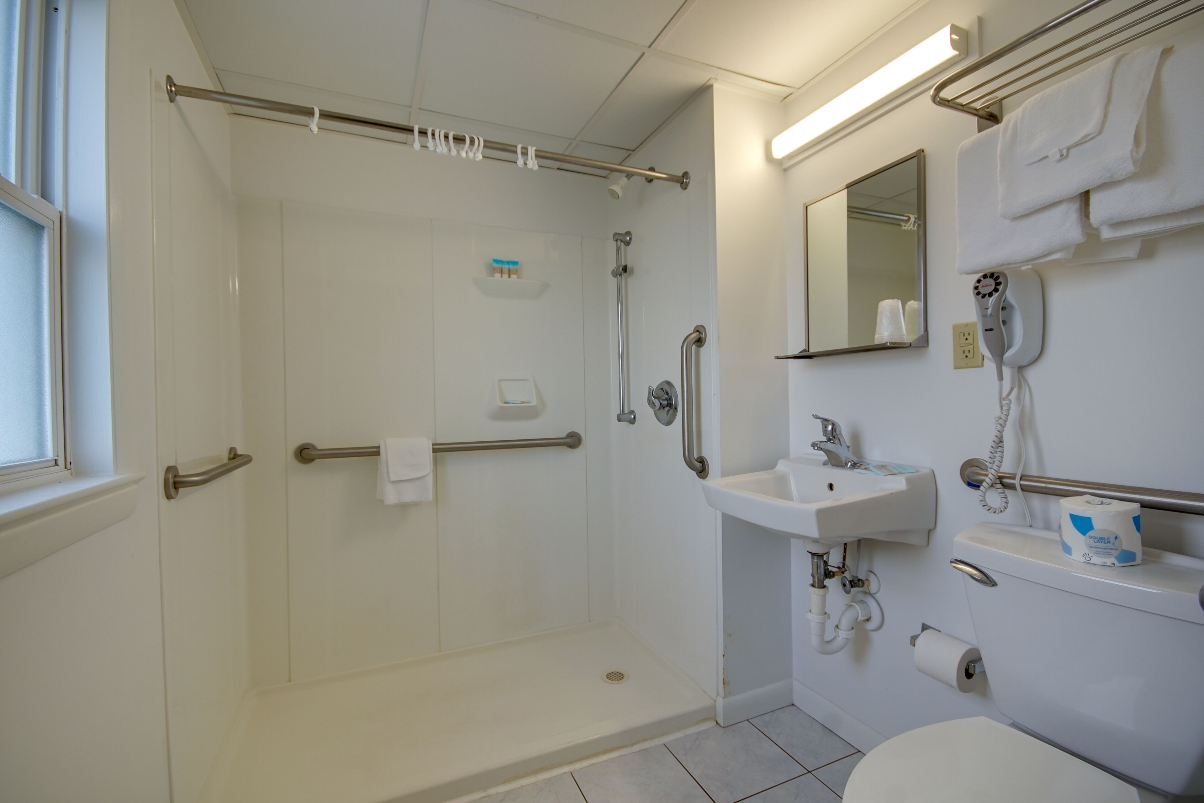A modern bathroom with a walk-in shower, grab bars, a sink, and a toilet.
