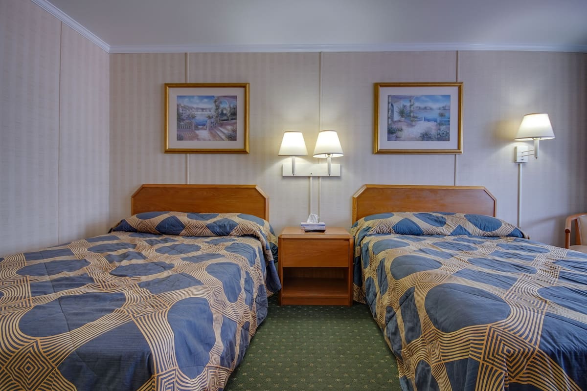 A hotel room with two single beds, a nightstand with lamps, and two framed pictures on the wall.