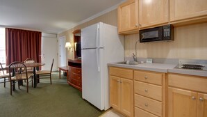 A compact kitchen with wooden cabinets, a white refrigerator, a microwave, and a dining area with chairs and a table. - Sahara Motel (Ocean City)