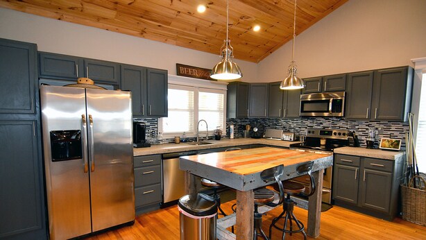 A modern kitchen with stainless steel appliances, wooden flooring, and a central island with stools.