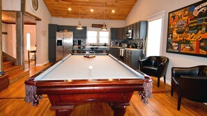 A pool table in a room with wooden flooring and a high ceiling.