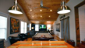 A spacious living room with a pool table, wooden ceiling, and a television in the background.