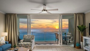 Ein Balkon mit Blick auf den Sonnenuntergang über dem Meer, ein Deckenventilator und eine Sitzecke mit Couchtisch und Sofa.