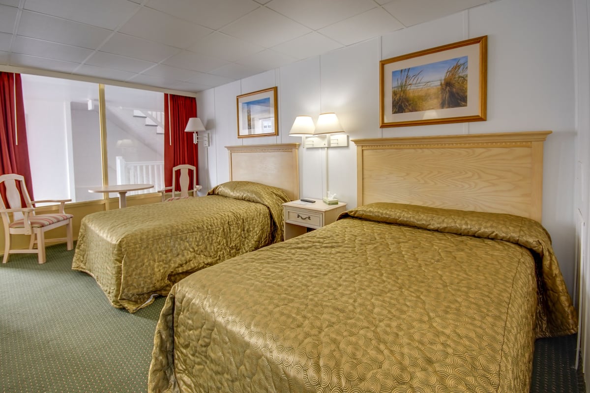 A hotel room with two beds, a desk, a chair, a lamp, and a painting on the wall.