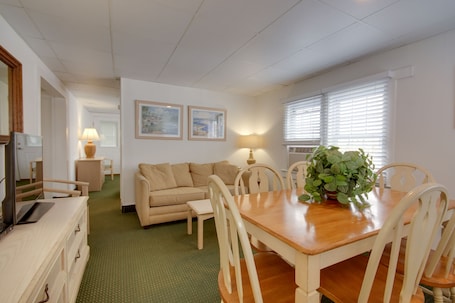 A room with a wooden dining table, beige sofa, and a TV on a wooden cabinet.