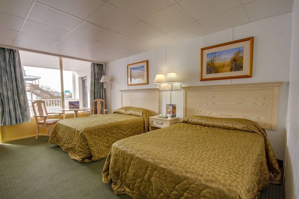 A hotel room with two beds, a desk, a chair, a window with curtains, and a painting on the wall.