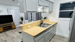 Uma cozinha compacta com bancada de madeira, pia de aço inoxidável e armários cinzas.