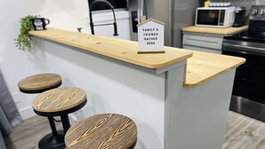 Uma cozinha com ilha de madeira, dois banquetes e uma placa que diz 'Família e Amigos se Reúnem Aqui'.