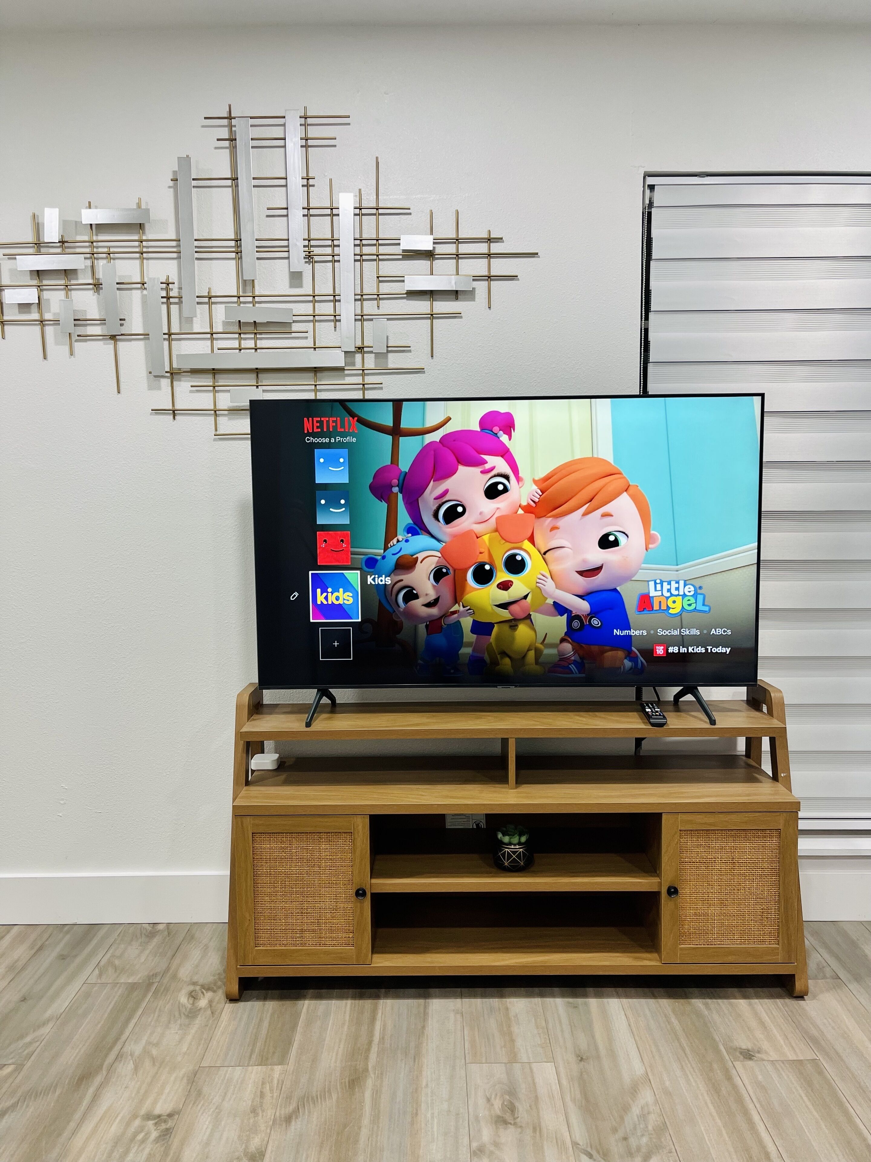 Een televisie op een houten standaard, met daarboven een decoratief kunstwerk aan de muur.