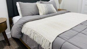 Cama bem arrumada com roupa de cama cinza e manta branca.