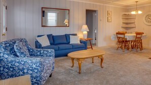 A living room with a blue sofa, a wooden coffee table, a dining table with chairs, and a lamp. - Ocean Terrace Family Apartments (Ocean City)