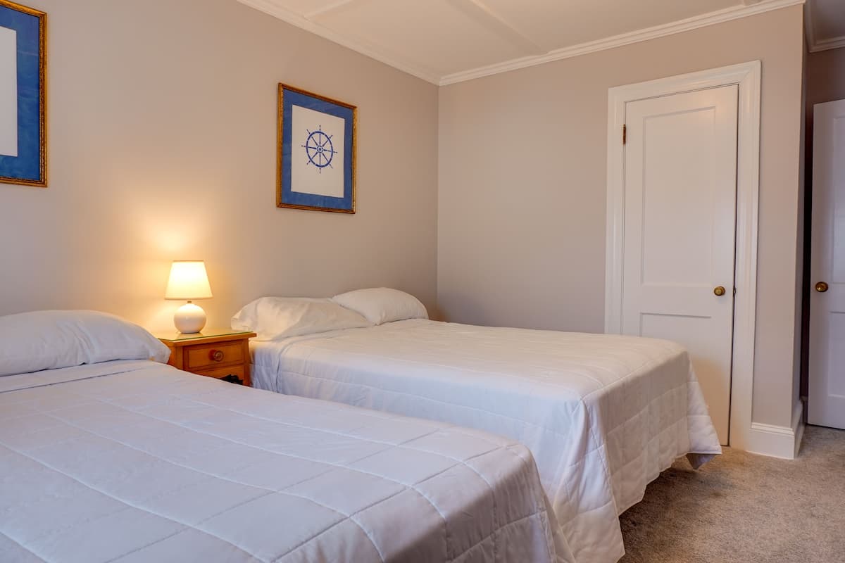 A hotel room with two beds, a nightstand with a lamp, a framed picture on the wall, and a closed door.