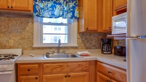 A kitchen with wooden cabinets, a stainless steel sink, a stove, a microwave, and a coffee maker. - Ocean Terrace Family Apartments (Ocean City)