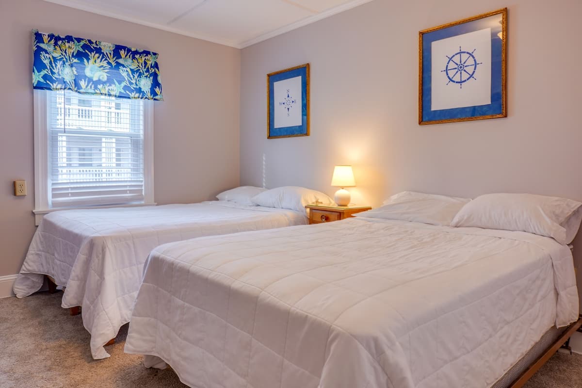 A room with two single beds, a window with blinds, a wall-mounted compass picture, and a bedside lamp.