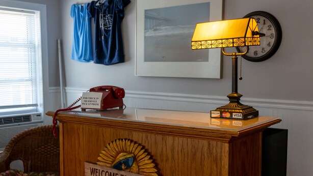 A reception desk with a wooden sign reading "WELCOME TO THE BEACH," a red telephone, a lamp, and a clock on the wall.