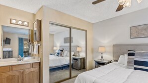 A hotel room with a large mirror, a vanity with a sink, a bed with white bedding, and a bedside table with a lamp. - Contemporary Country Club Condo with portable A/C's in the bedrooms. (Flagstaff)