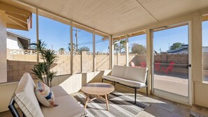 Eine sonnendurchflutete Terrasse mit einer Couch, einem runden Tisch und einem Blumentopf.