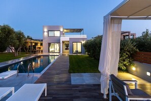 A modern two-story house with a swimming pool, outdoor seating, and a covered patio area.