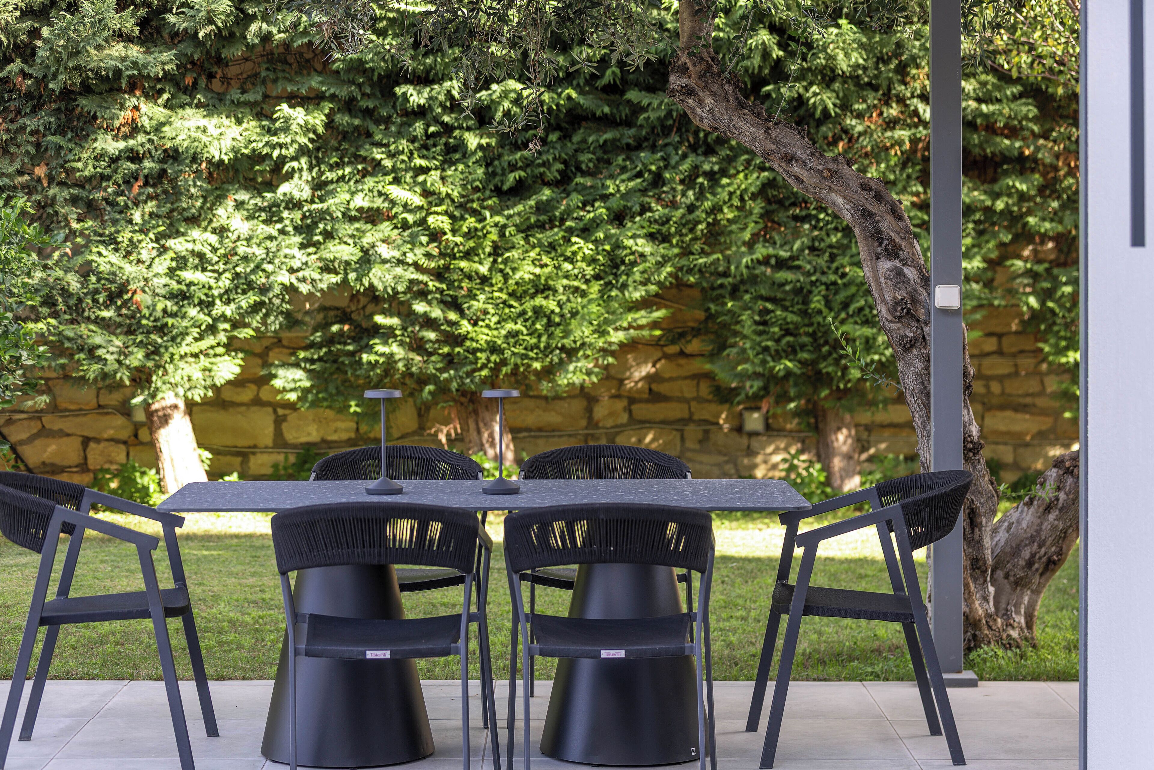 A patio with a table and chairs, surrounded by a stone wall and lush greenery.
