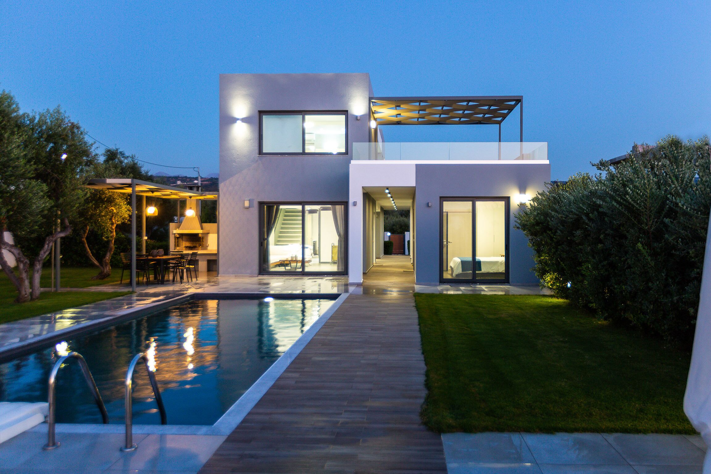 A modern two-story house with a swimming pool, outdoor seating, and a well-maintained lawn.