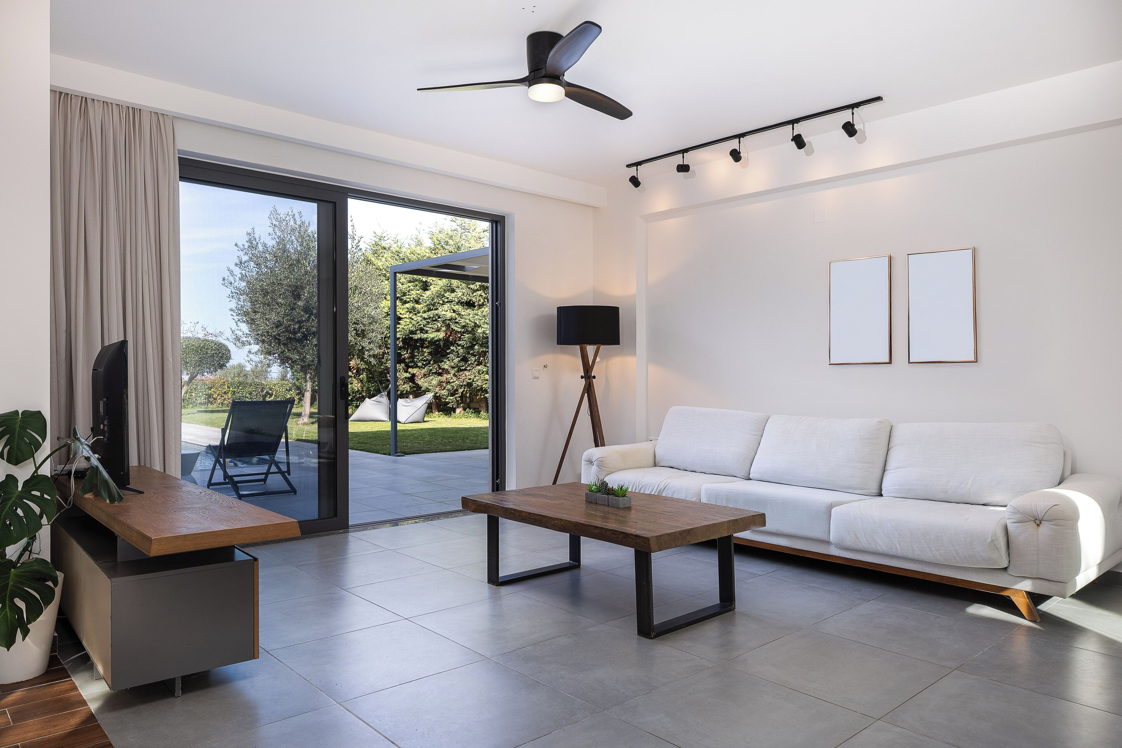 Een moderne woonkamer met een witte bank, een houten salontafel, een tv op een standaard, een vloerlamp en een plafondventilator.