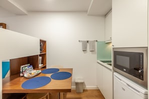 Cocina pequeña equipada con microondas, fregadero y un pequeño bote de basura. Se ve una mesa de madera con manteles individuales azules y una bandeja de aperitivos.