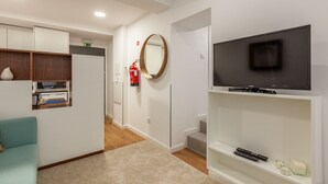 A hotel room with a television on a stand, a mirror, a sofa, and a small shelf with a remote control. - Underground Batalha Studios - A (Oporto)