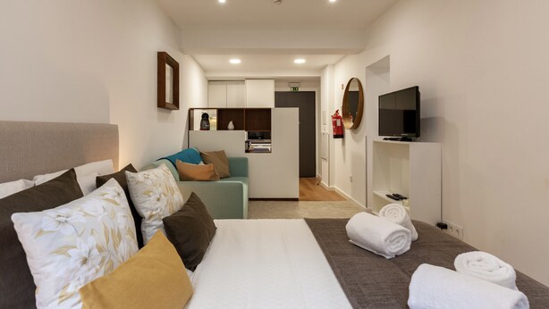 A hotel room with a bed, a sofa, a TV, and a bathroom visible in the background. - Underground Batalha Studios - A (Oporto)