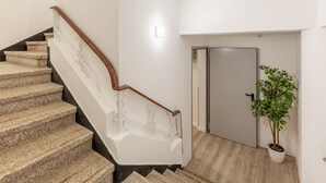 A staircase with a wooden handrail and beige steps, leading to a door with a potted plant beside it. - Underground Batalha Studios - B (Oporto)