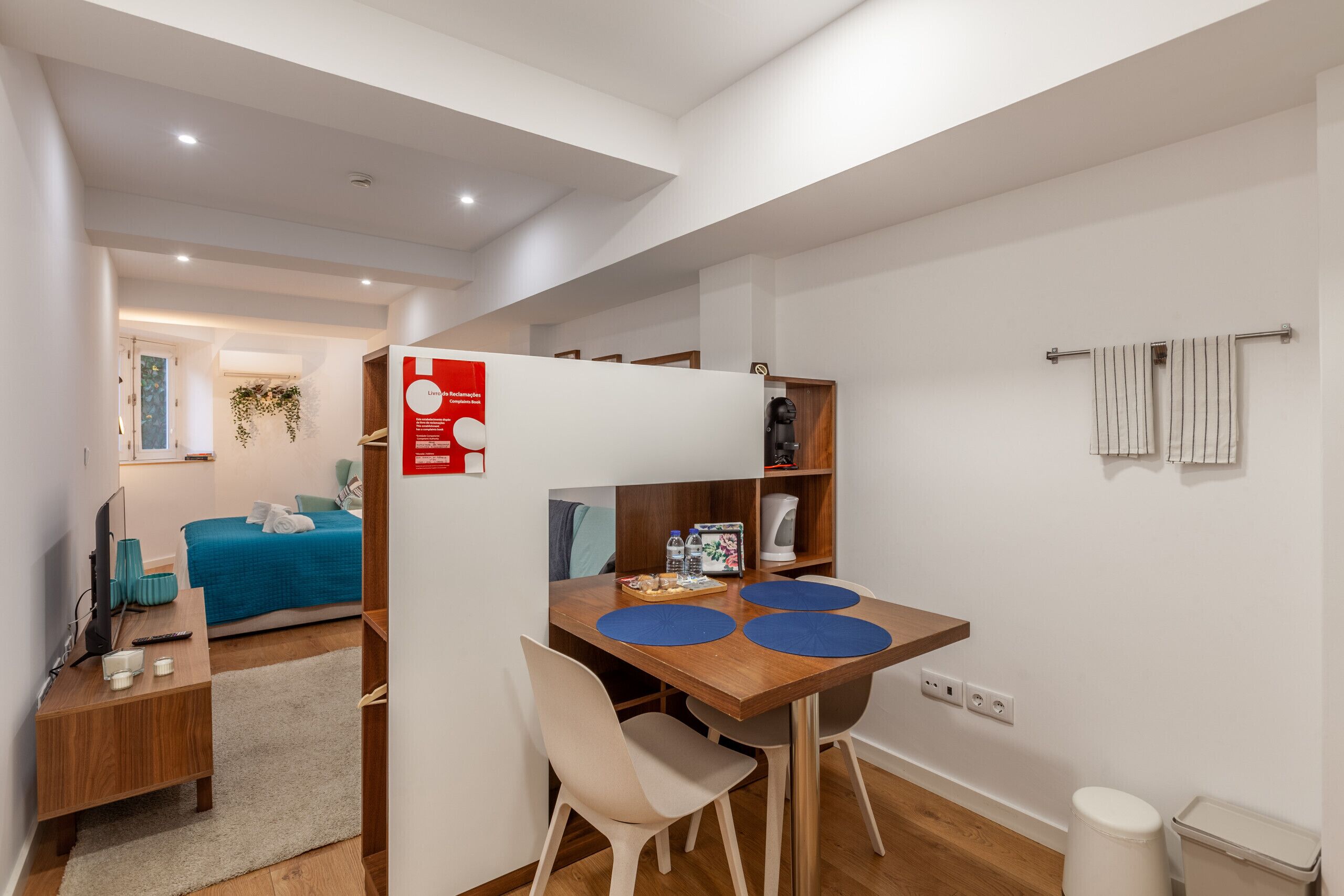 A compact hotel room with a kitchenette, a bed, a small dining area, and a bathroom.