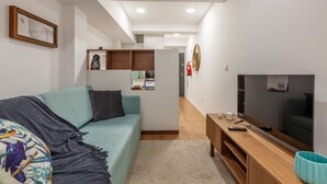 A modern living room with a teal sofa, a wooden coffee table, a flat-screen TV, and a kitchen area in the background. - Underground Batalha Studios - C (Oporto)