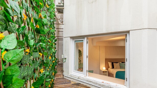 A narrow wooden pathway leading to a room with a large window, a bed, and a bedside table with a lamp. - Underground Batalha Studios - C (Oporto)