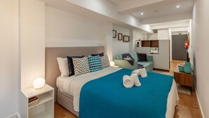 A modern hotel room with a large bed, a bedside table with a lamp, a chair, and a small desk with a lamp. - Underground Batalha Studios - C (Oporto)