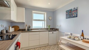 A modern kitchen with white cabinets, a wooden countertop, a dishwasher, and a dining area with a bench. - 3 bedroom accommodation in Porthleven (Porthleven)