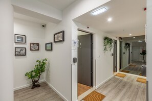 A hallway with white walls, framed artwork, a potted plant, and a door leading to another room.