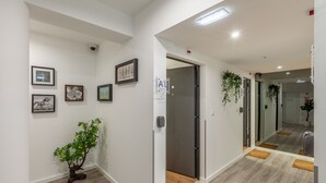 A hallway with white walls, framed artwork, a potted plant, and a door leading to another room. - Underground Batalha Studios - E (Oporto)