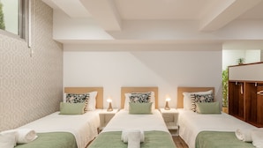 A hotel room with three single beds, each with a green bedspread and white linens, and a wooden headboard. There are bedside tables with lamps and a small plant on one side. - Underground Batalha Studios - E (Oporto)