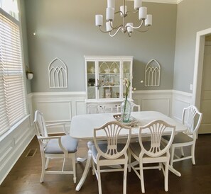 A beautifully appointed dining room with a white table and six chairs, a chandelier, and decorative molding accents.