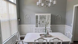 A dining room with a large white table, six white chairs, a chandelier, and decorative window shutters. - 2026 Master’s Rental, 3 Story with pool—Just 12 Miles from the Augusta National (Evans)
