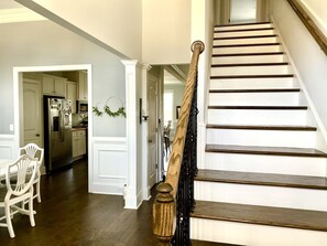 Staircase leads to an upper level, with a dining area below featuring a white table and chairs.