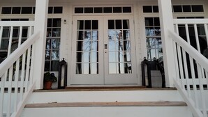 Eine weiße Veranda mit Doppeltür, zwei Laternen und einem Deckenventilator.