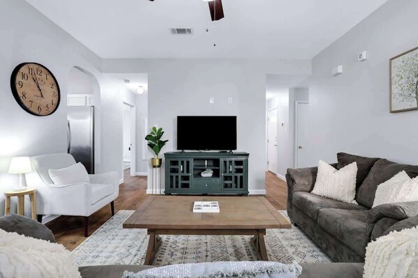 Una sala de estar con televisor, sofá, mesa de centro y un reloj en la pared.