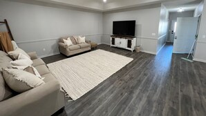 Un ampio soggiorno con un grande tappeto bianco, un divano color beige, una televisione a schermo piatto e una ventola a soffitto.
