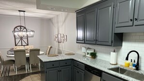 Una cucina moderna con mobili grigio scuro, un piano di lavoro in granito e una lavastoviglie. C'è una zona pranzo con un lampadario e un tappeto.