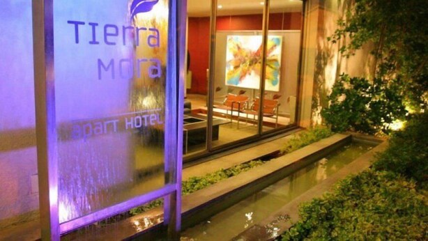 A modern hotel with a glass facade, a visible pool area, and a seating area with chairs.