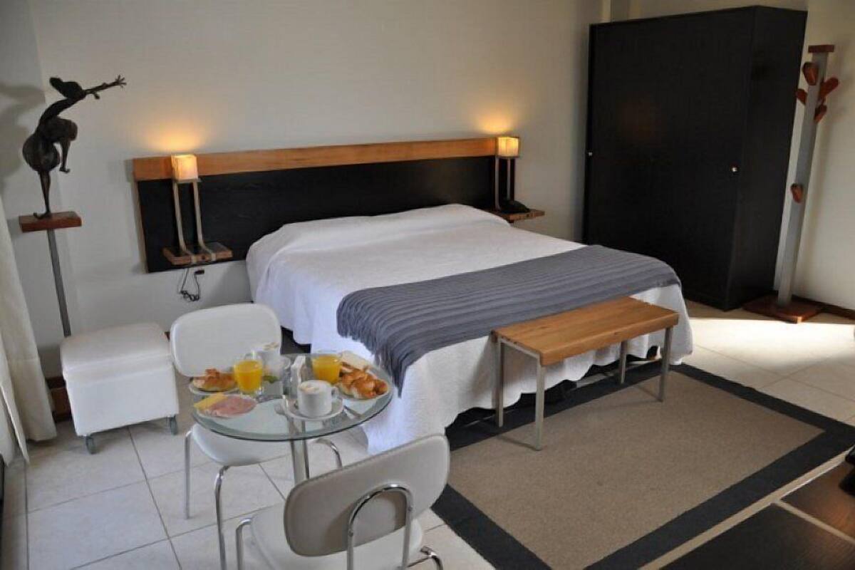 A hotel room with a bed, bedside tables, a small table with breakfast, a chair, and a wardrobe.