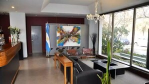 A modern lobby with a reception desk, seating area, and large windows offering a view of the street.