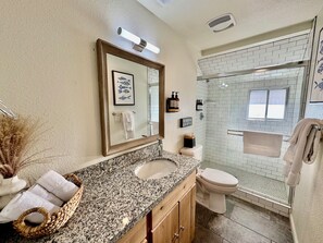 A bathroom with a granite countertop, a sink, a toilet, and a glass shower enclosure. - Adventure Lodge (South Lake Tahoe)