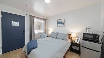 A hotel room with a bed, a desk with a lamp, a microwave, and a refrigerator.