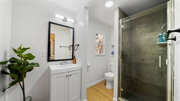 A bathroom with a white sink, mirror, toilet, and a glass-enclosed shower.
